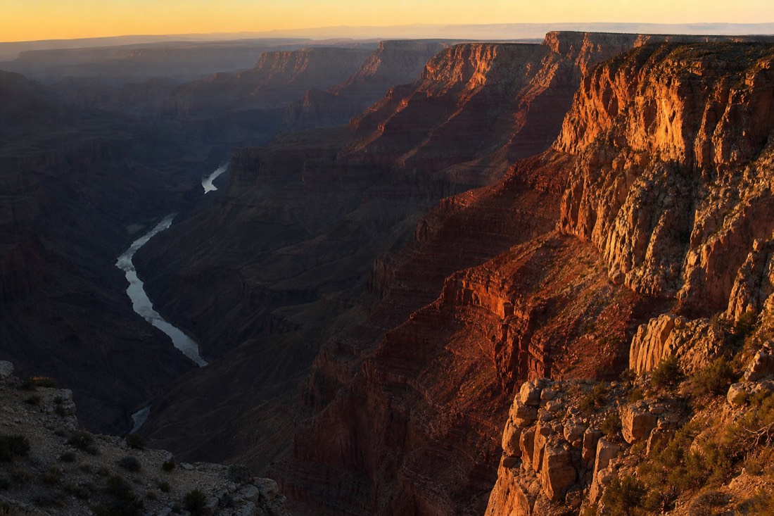 Low golden light cutting across canyon buttes and casting long shadows into the gorge at the end of the day