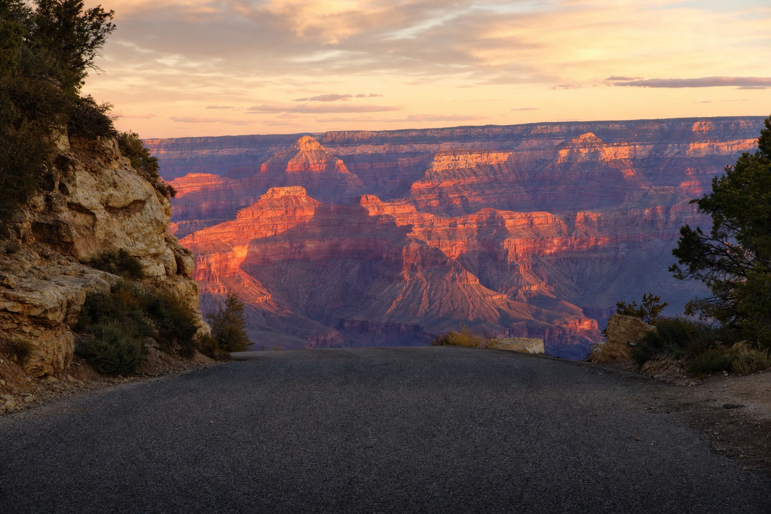 The Grand Canyon glowing at sunset beyond an open entrance road with no barriers in sight