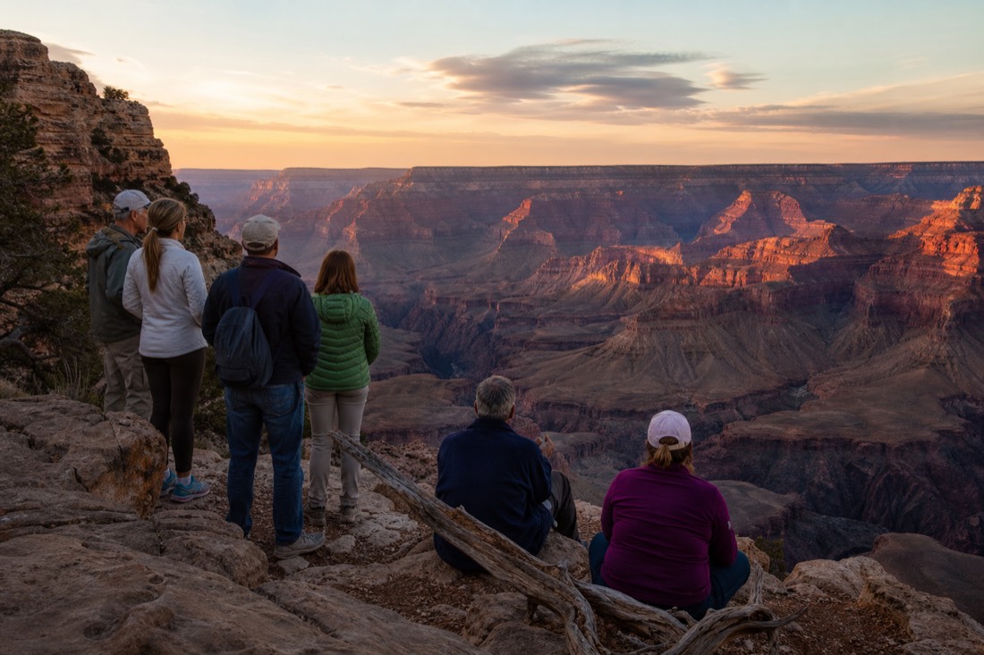 A small tour group watching sunset colors flood the canyon from a quiet stone overlook away from the crowds