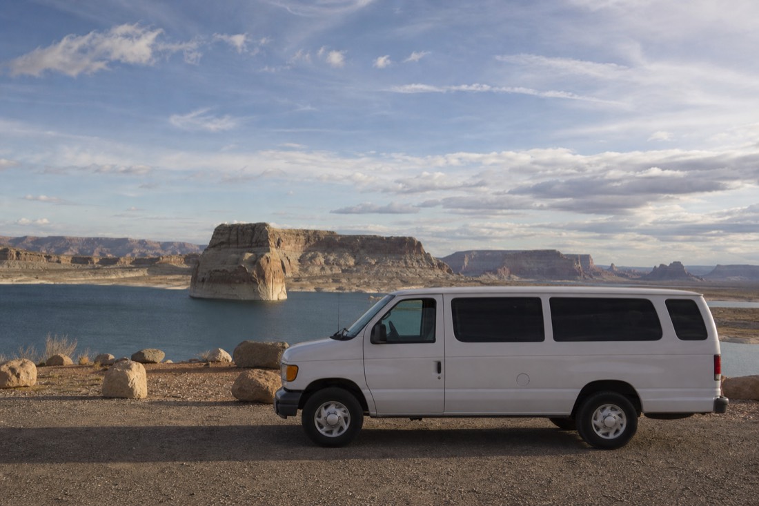 A small-group tour van at a Lake Powell overlook with sandstone domes and blue water behind