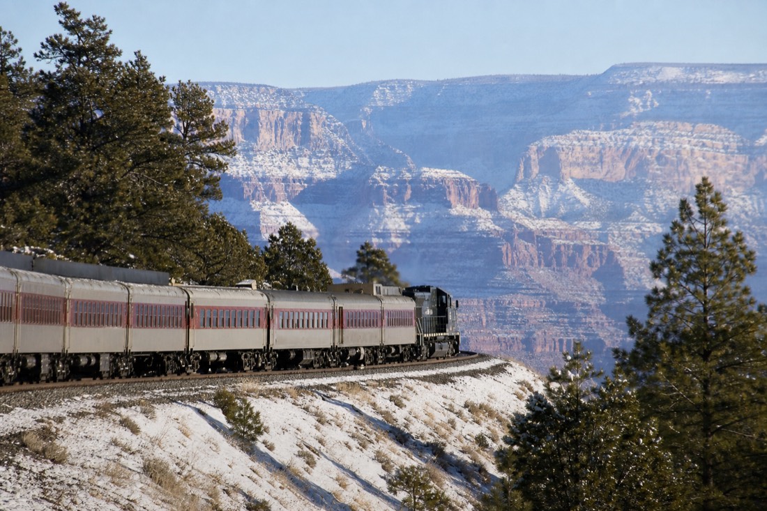 A vintage passenger train crossing snowy pine country between Williams and the Grand Canyon on a bright winter day
