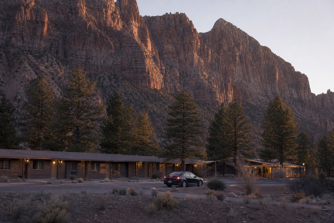 A small motel strip near the park gate at dusk with pines behind and a car pulling into the lot