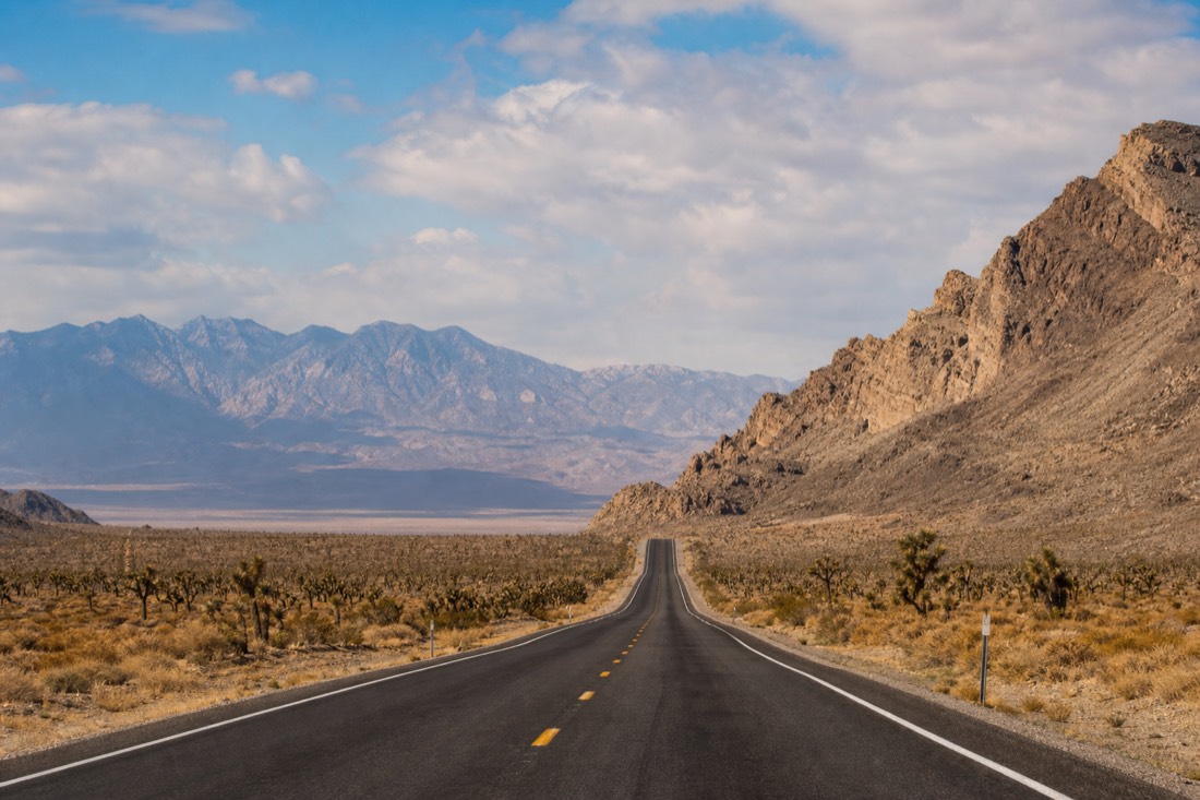 Empty desert highway heading east from Las Vegas through Joshua trees toward distant mountains
