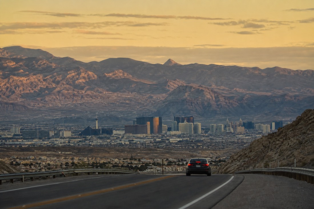 Pre-dawn light over a quiet Las Vegas street with a car heading east away from the hotel towers