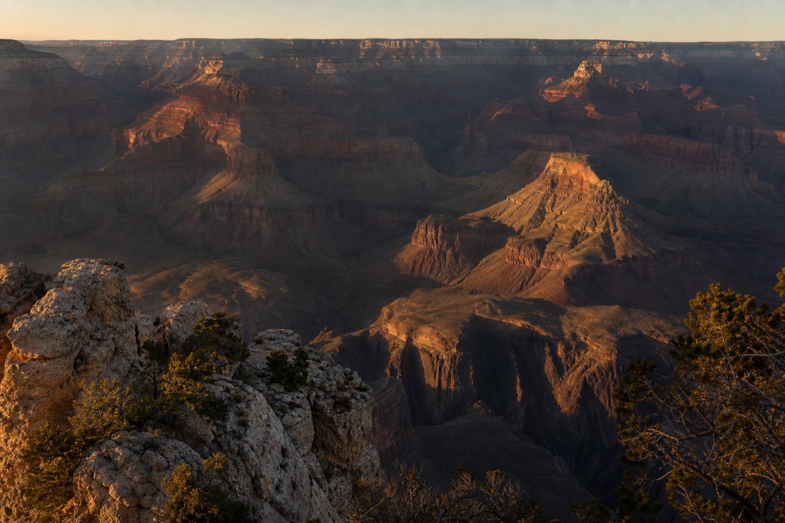 Late afternoon shadows stretching across the South Rim as visitors gather along a stone parapet before sunset