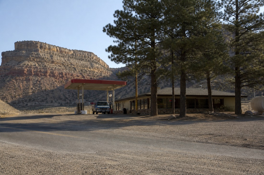 A small roadside fuel station and diner under pine trees on the high plateau with a pickup truck at the pump