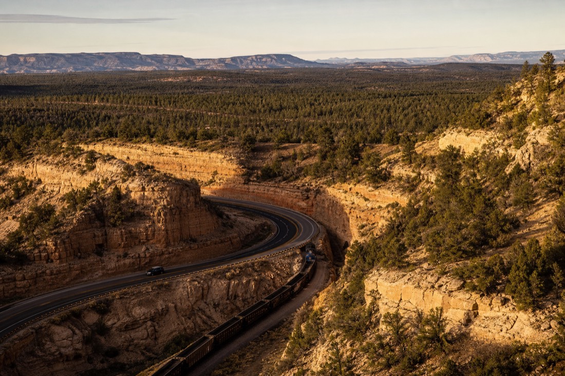 A car and a train seen from a high vantage point on the Arizona plateau with pine forest stretching to the horizon
