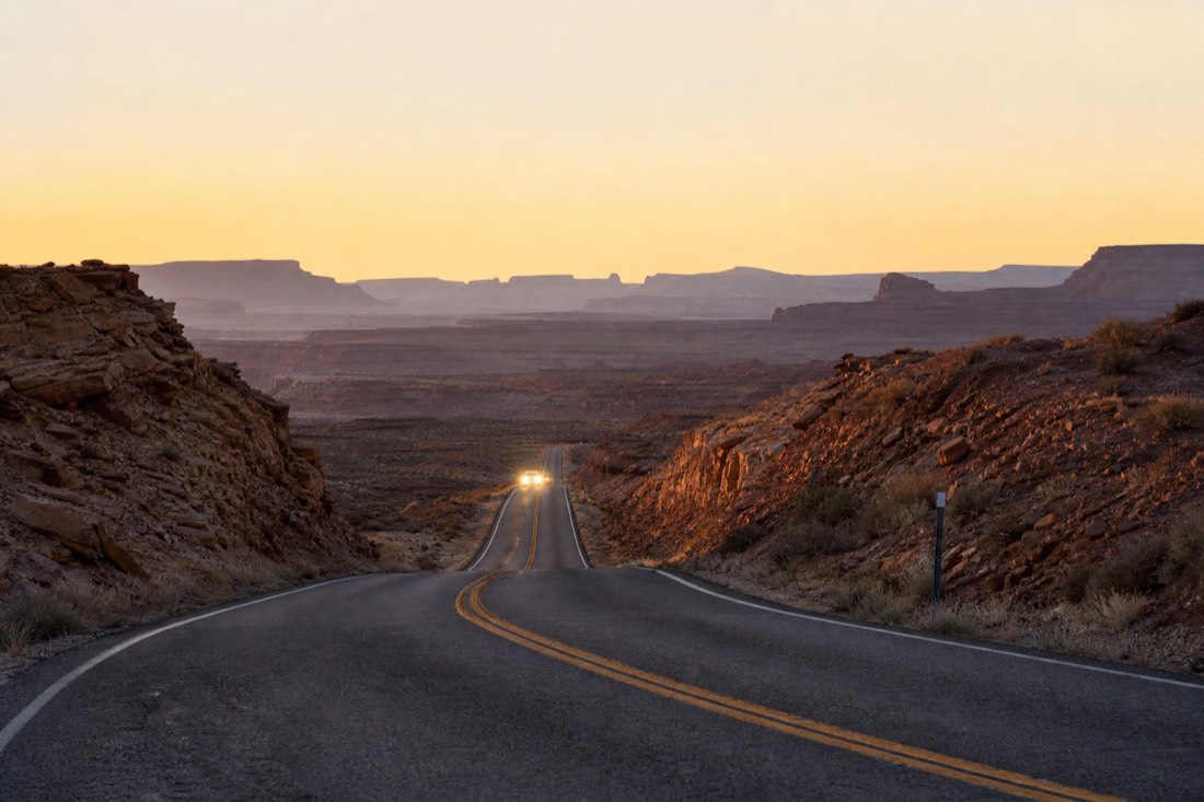 Empty highway at dusk on the high plateau with headlights approaching and the last light behind distant hills
