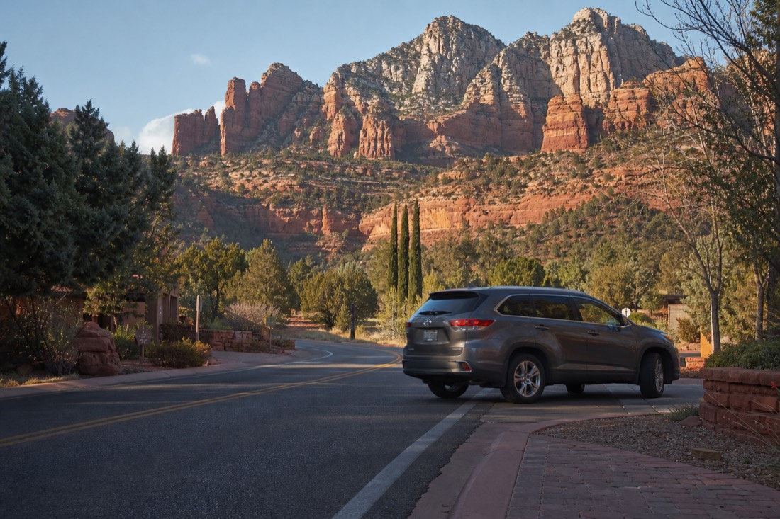 Morning light on a quiet Sedona street with red rock walls behind and a car pulling out toward the highway