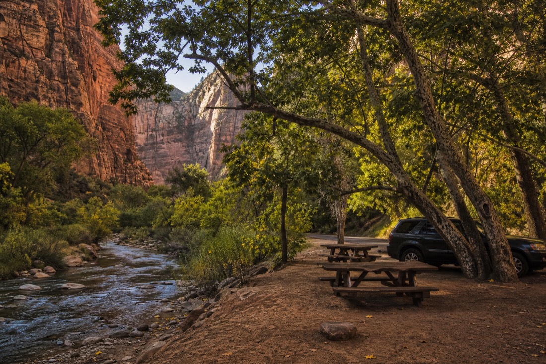 A creekside pull-off in Oak Creek Canyon with picnic tables under sycamores and a parked car