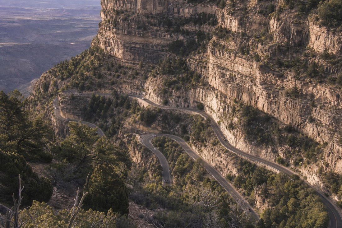 Tight hairpin bends of a forest highway seen from above, cut into a steep wooded canyon wall