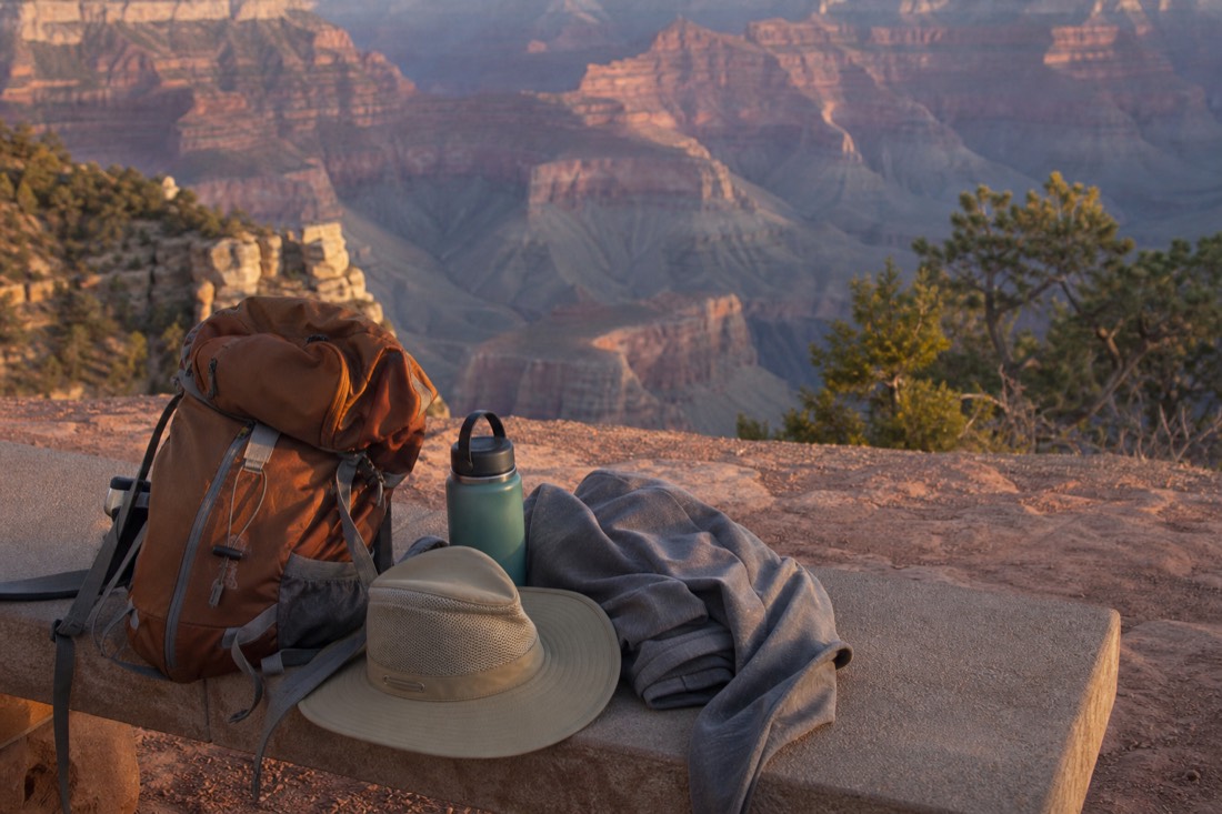 A daypack, wide-brimmed hat, water bottle and light fleece laid out on a bench beside a canyon overlook
