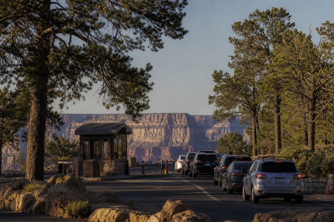 The South Rim entrance station with a ranger booth and a line of cars under tall ponderosa pines