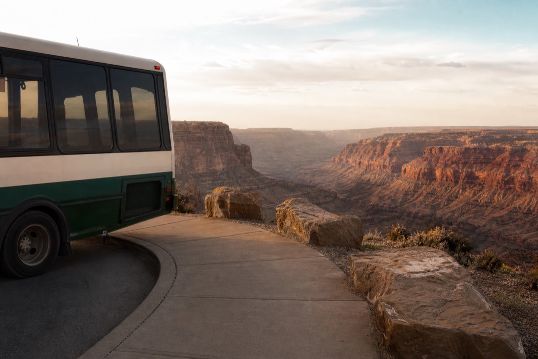 A shuttle bus pulling up at a level viewing area above the western canyon with a paved boarding kerb
