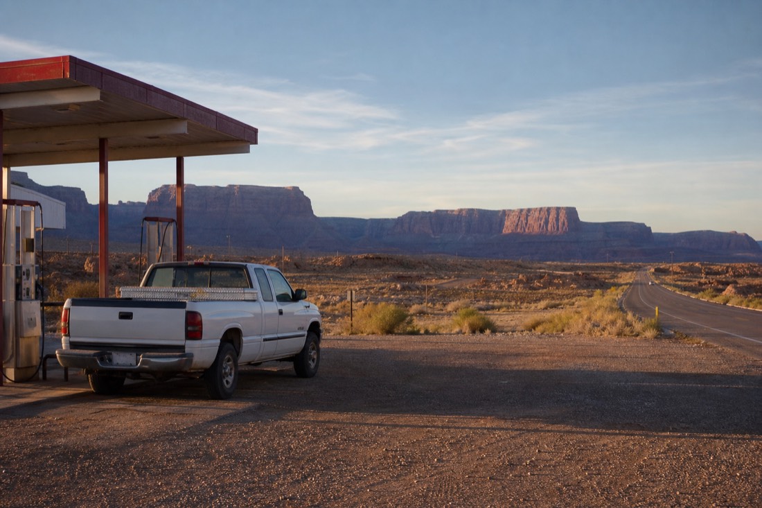 A pickup truck at a remote desert gas station on a long Arizona highway with red mesas on the horizon