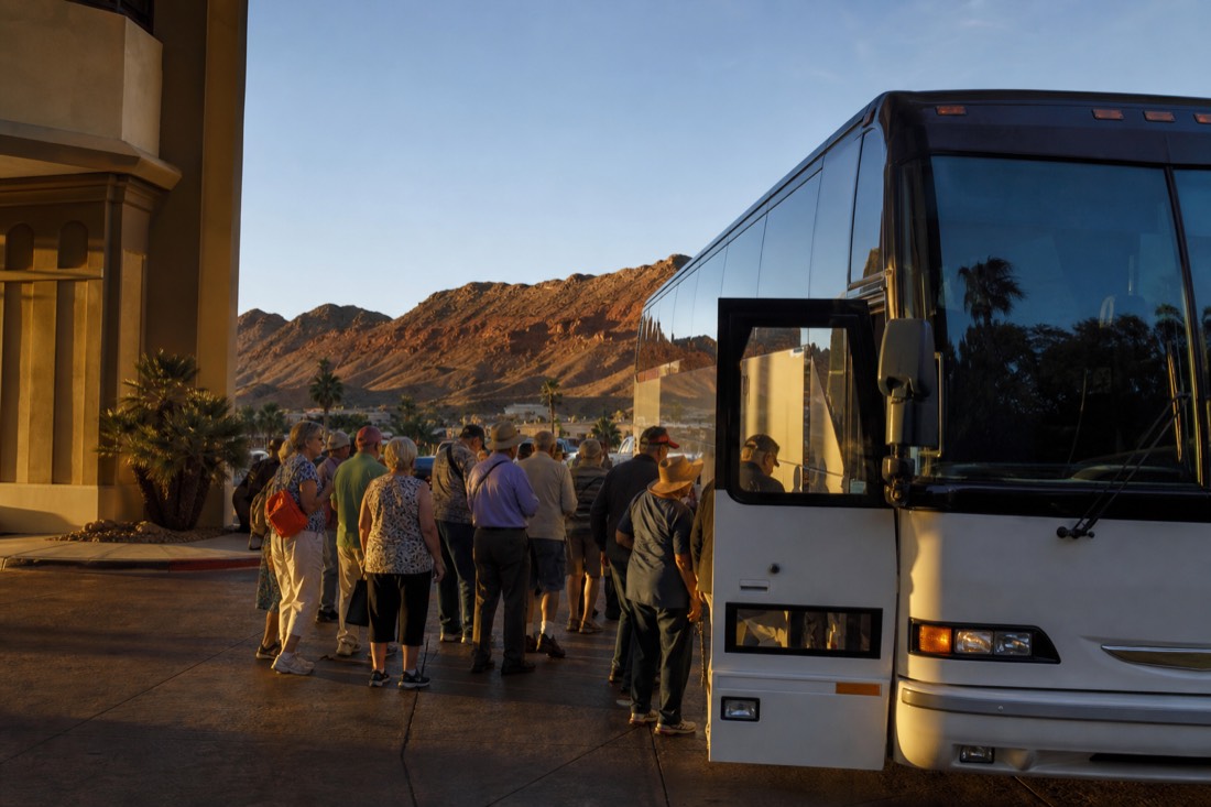 Passengers boarding a tour coach outside a Las Vegas hotel entrance in early morning light