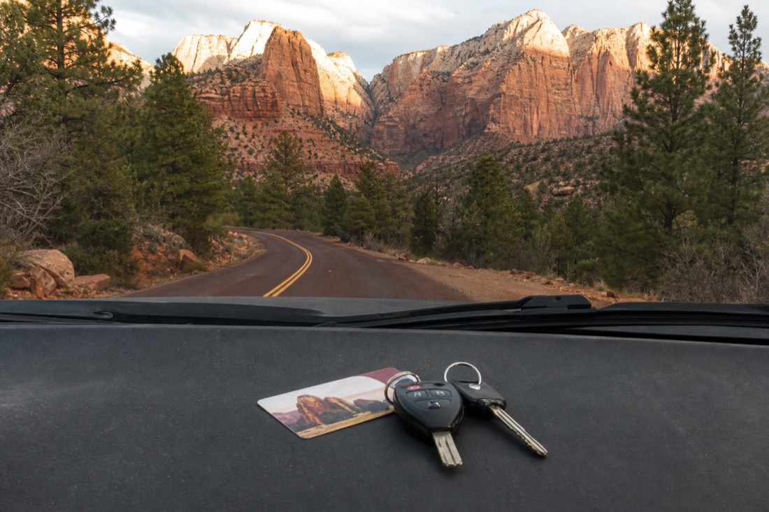 An annual national park pass and car keys resting on a dashboard with a pine-lined park road ahead