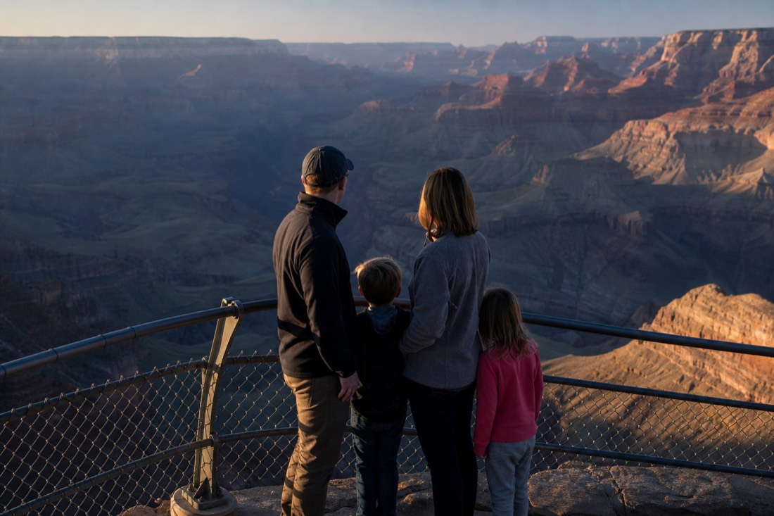 A family standing at a railed overlook in early morning light with the canyon still half in shadow