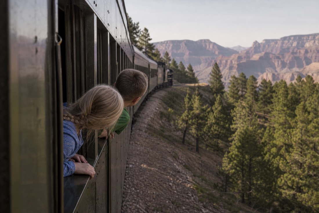 Children leaning at a vintage train window watching pine forest roll past on the way to the Grand Canyon