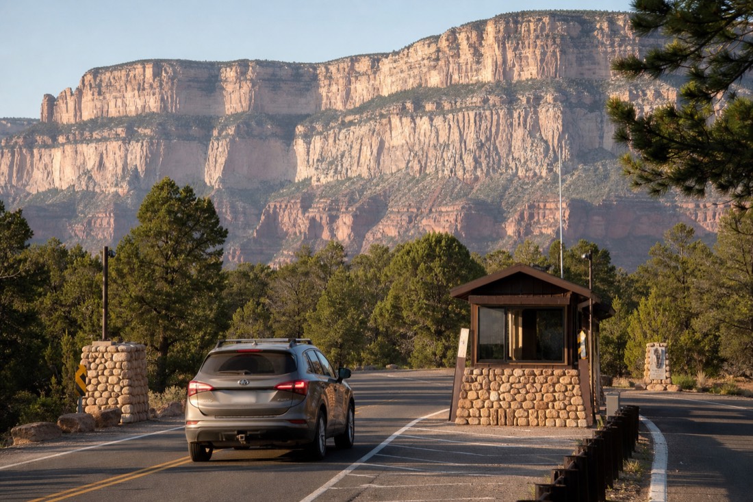 A family car waiting at the Grand Canyon entrance station with a ranger booth and pine forest behind