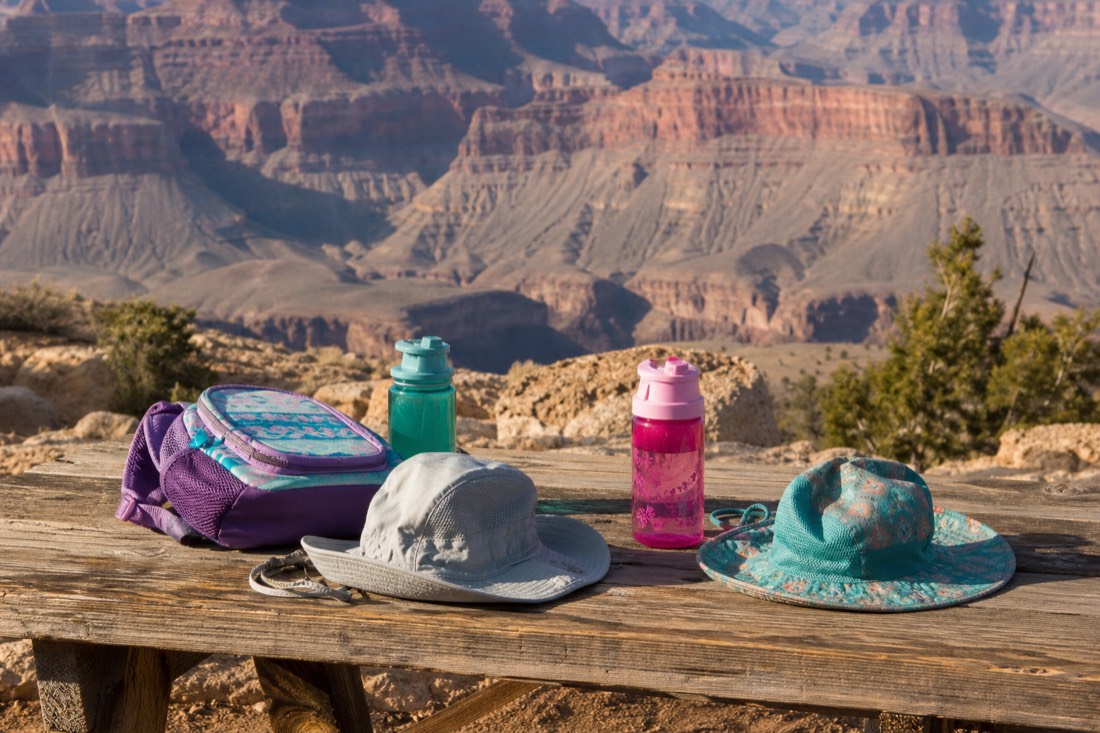 Kid-sized sun hats, water bottles and a small backpack on a picnic table near the canyon rim