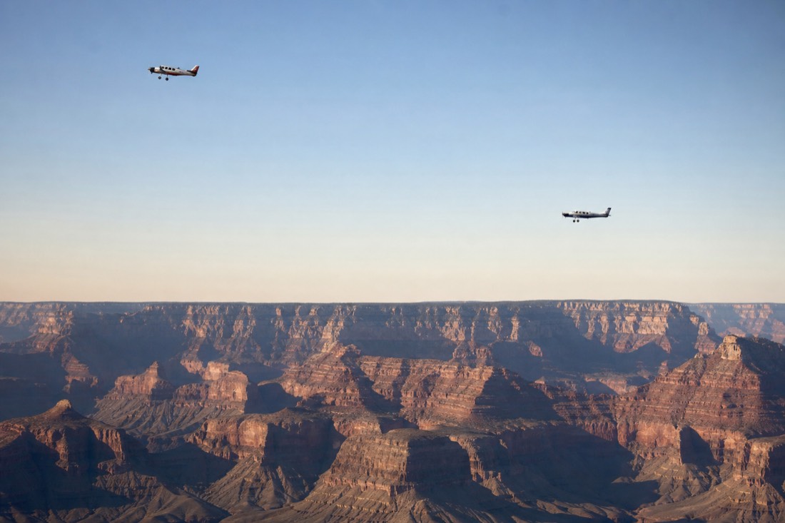 Two small aircraft holding separate altitudes above the canyon rim under a wide clear sky