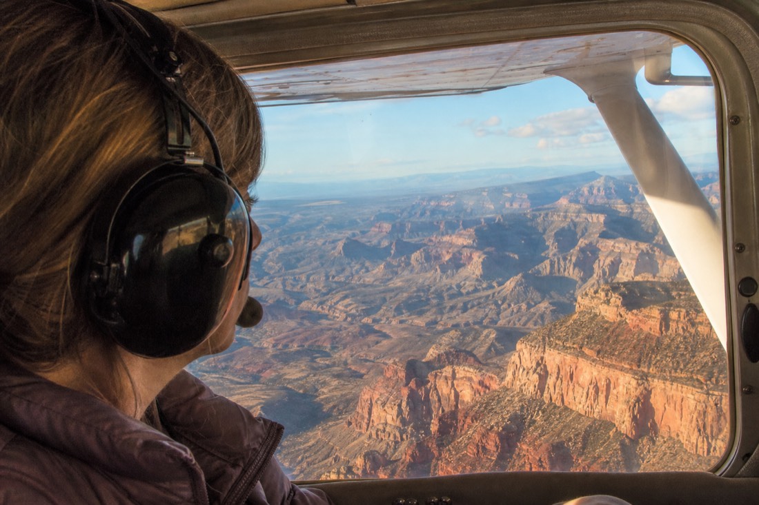 A passenger wearing an aviation headset looking out of a small aircraft window over red rock country