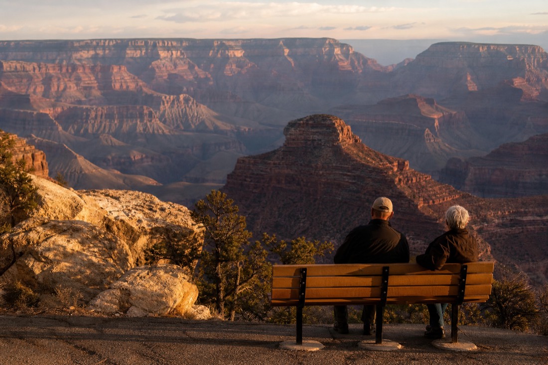 Warm evening light on canyon buttes seen from a quiet South Rim overlook with two people watching from a bench