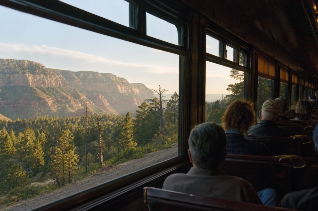 A vintage railway carriage interior with passengers looking out at pine forest on the way to the Grand Canyon