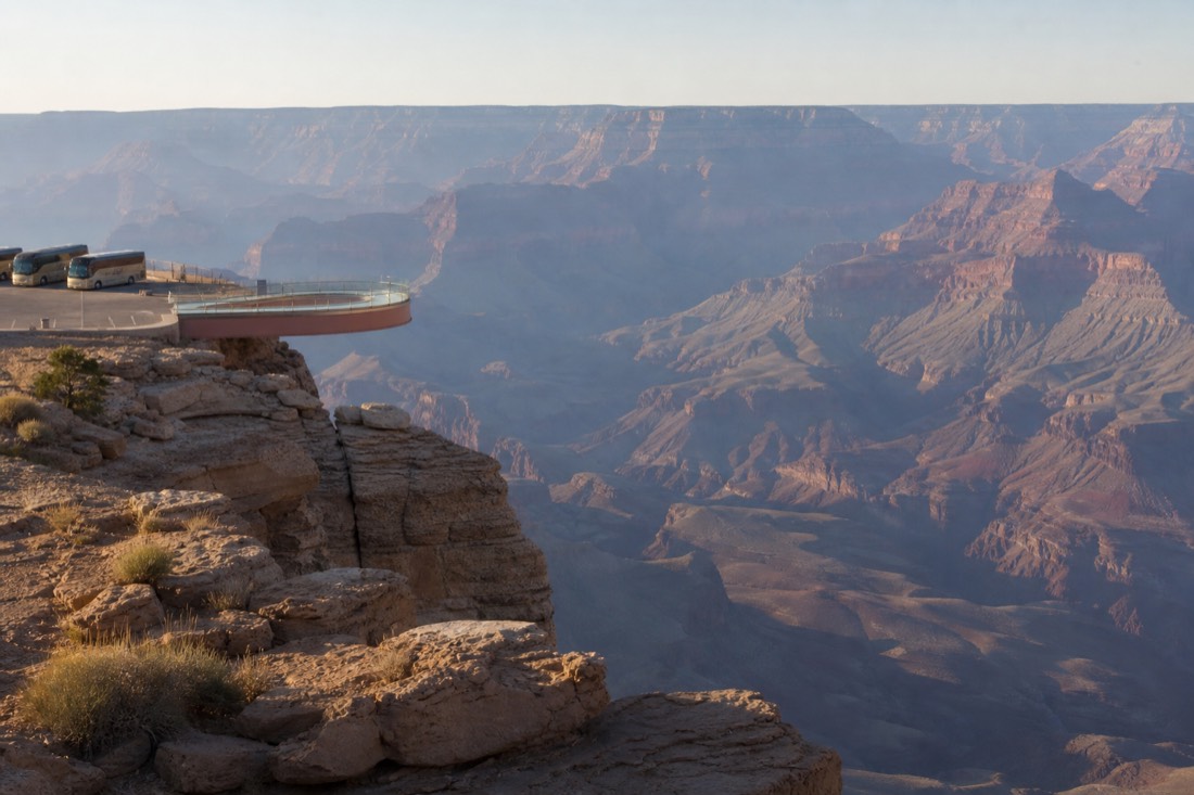 The glass Skywalk bridge curving out over the canyon rim at Grand Canyon West with shuttle buses waiting nearby