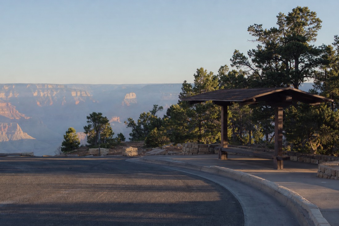 A nearly empty park shuttle stop at the Grand Canyon visitor center in early morning with pine forest behind