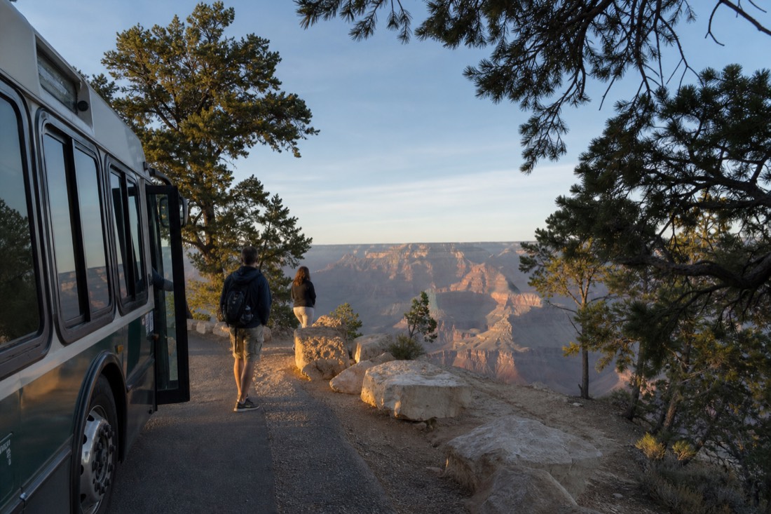 Visitors stepping off a free park shuttle bus at a pine-shaded rim viewpoint stop
