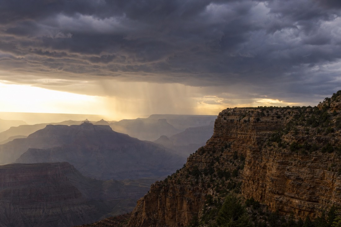 Dark monsoon thunderheads towering over the canyon with rain curtains falling in the distance