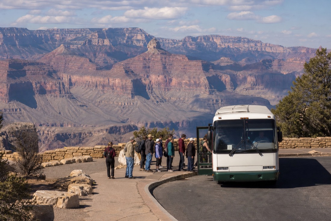 Visitors boarding a shuttle bus at a desert viewpoint plaza above the western Grand Canyon