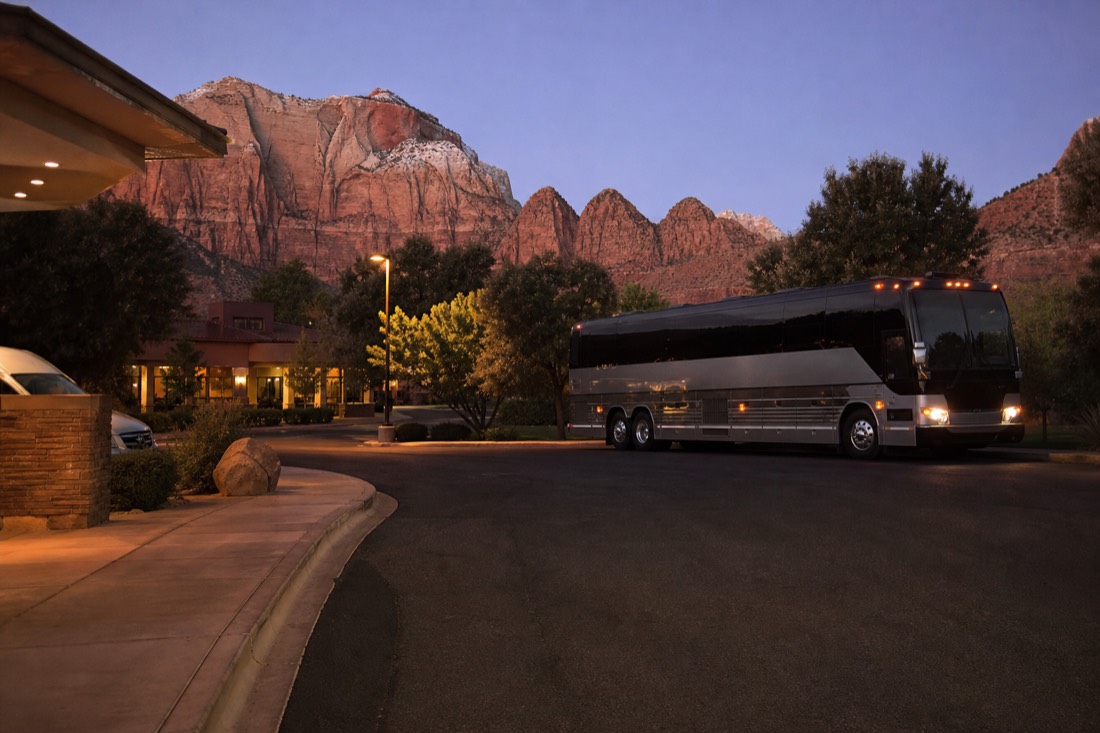 Predawn hotel pickup with a tour coach idling under streetlights and passengers boarding with coffee