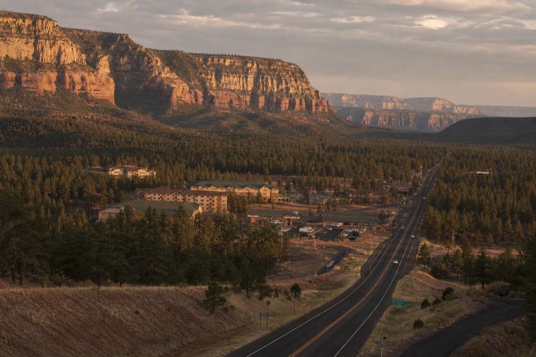Small hotel strip in Tusayan at dusk with pine forest on both sides of the highway toward the park gate