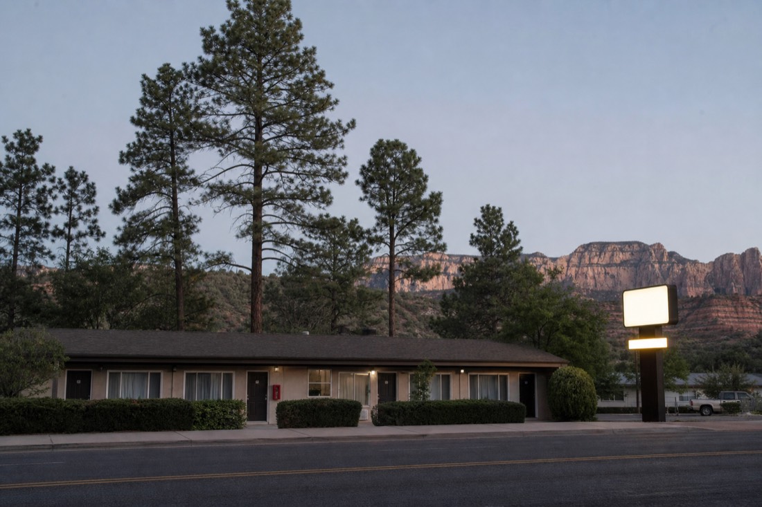 Ponderosa pines behind a low-slung motor lodge and a lit hotel sign on a quiet northern Arizona street